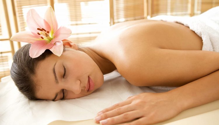 Mulher relaxando de bruços em maca de massagem com flor na orelha