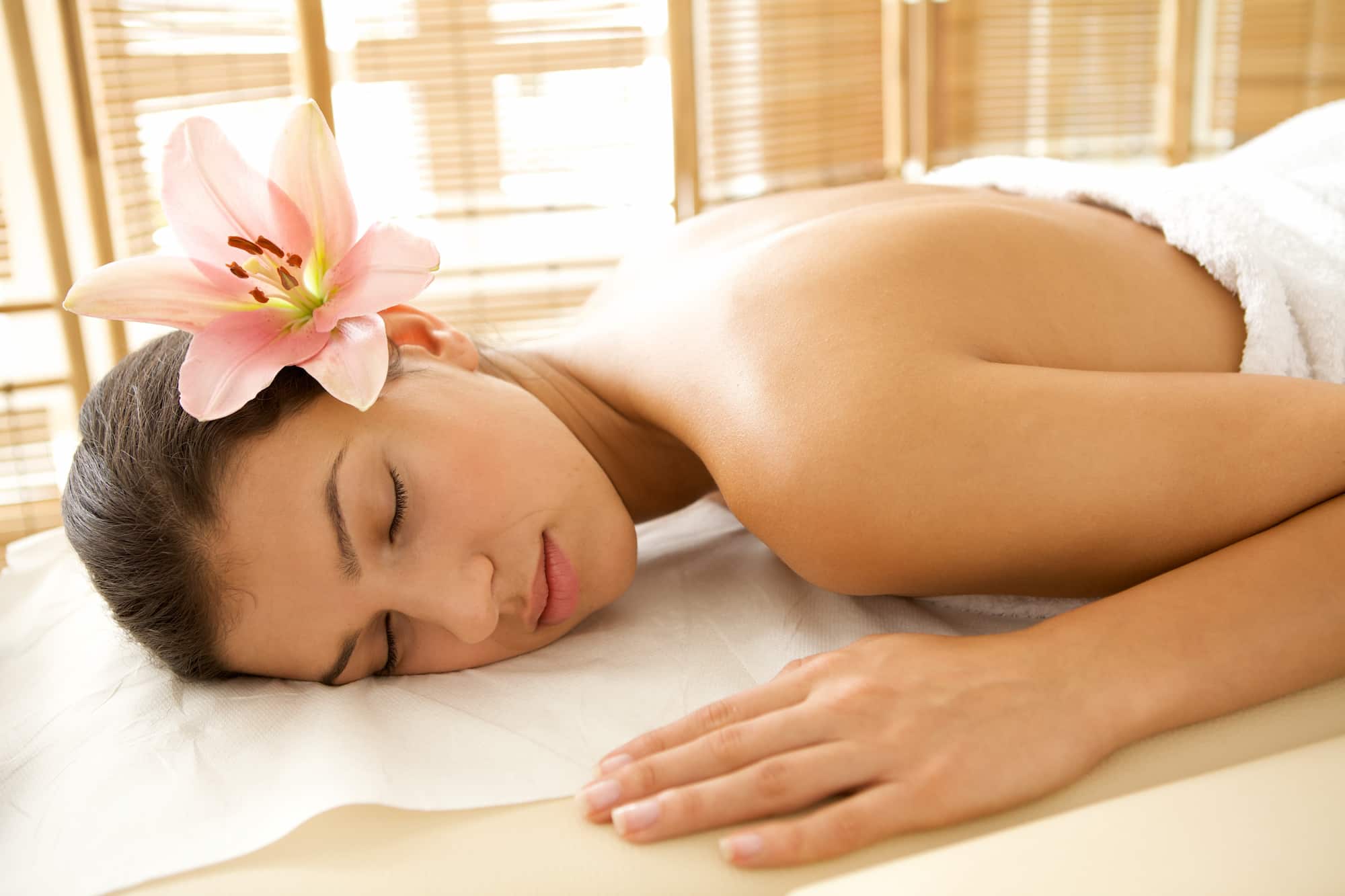 Mulher relaxando de bruços em maca de massagem com flor na orelha